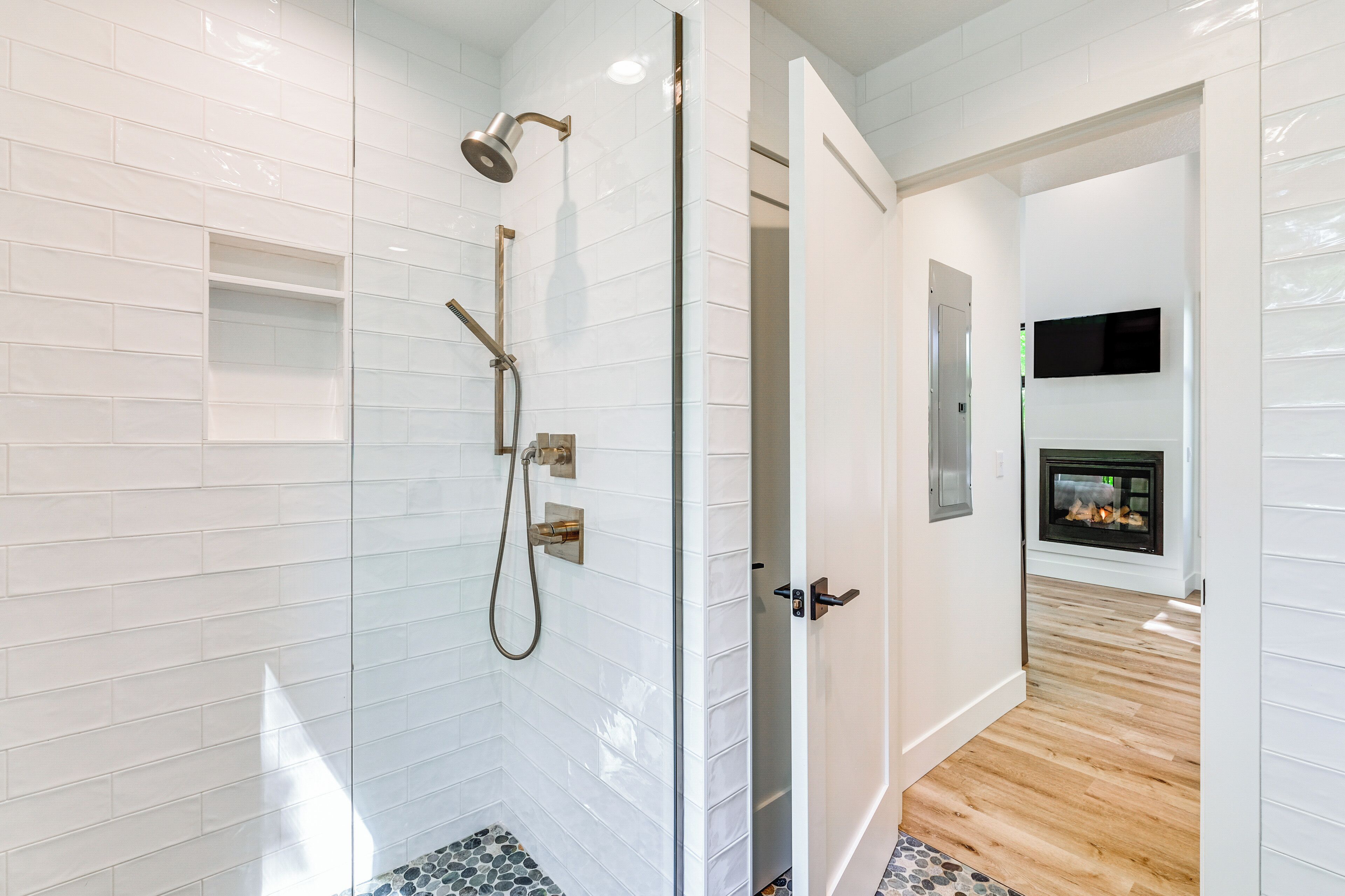 A modern bathroom with white subway tiles, a glass-enclosed shower, and a wooden floor.