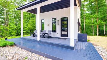 A covered outdoor area with a wooden deck, seating, and a door.