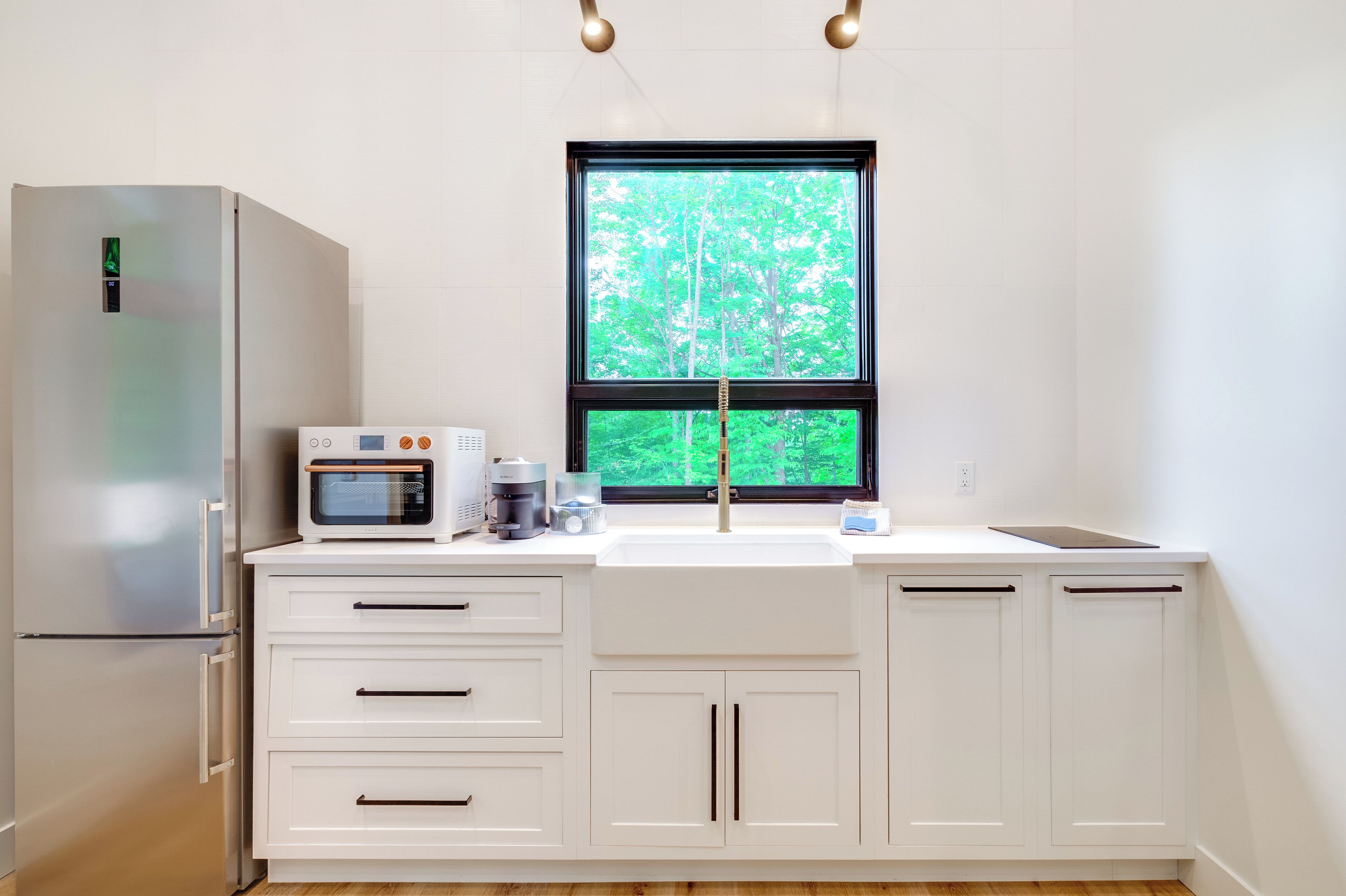 A modern kitchen with a built-in microwave, coffee maker, and a window with a view of trees.