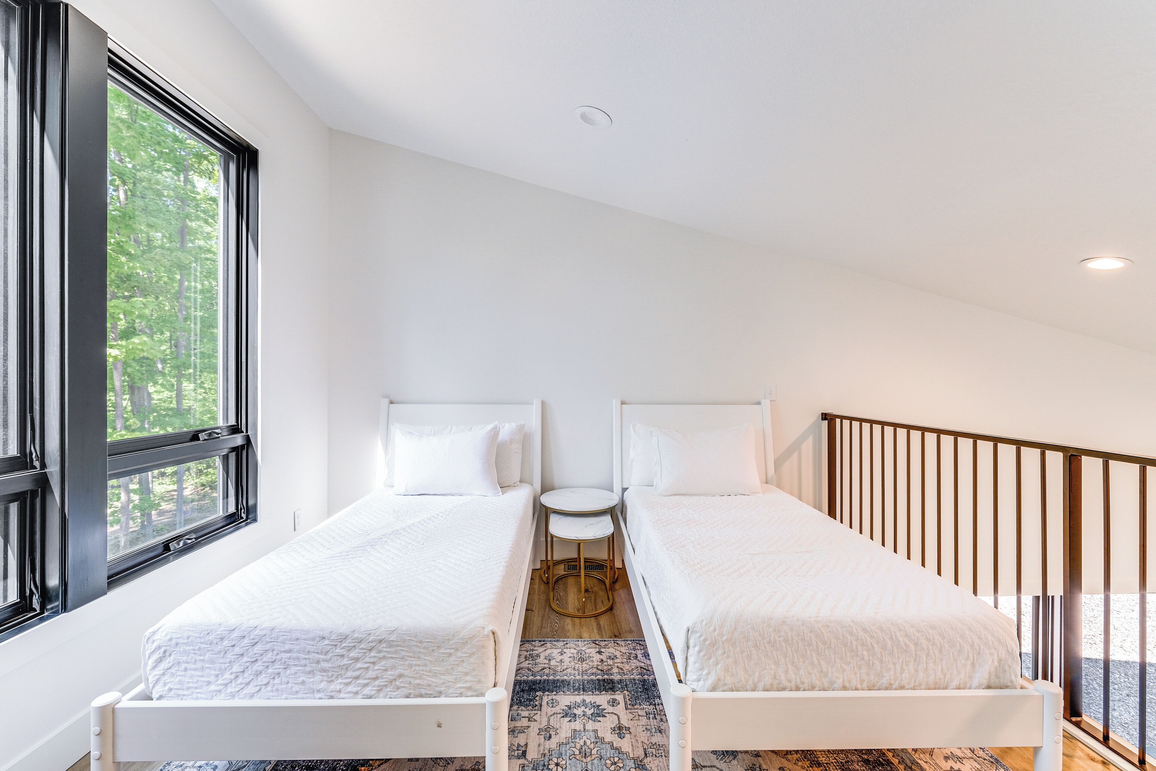 A bedroom with two single beds, a small round table, and a view of trees through a large window.