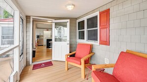 Una habitación con suelo de madera, un sillón tapizado de rojo, un banco de madera y una puerta que da a una zona de cocina.