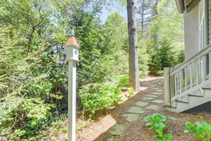 A stone pathway leading to a wooden staircase surrounded by lush greenery and a birdhouse. - Designer Cashiers Cottage, Perfect Porch, EV Plug (Cashiers)