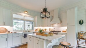 A spacious kitchen with white cabinetry, a large island with stools, and a hanging light fixture. - Designer Cashiers Cottage, Perfect Porch, EV Plug (Cashiers)