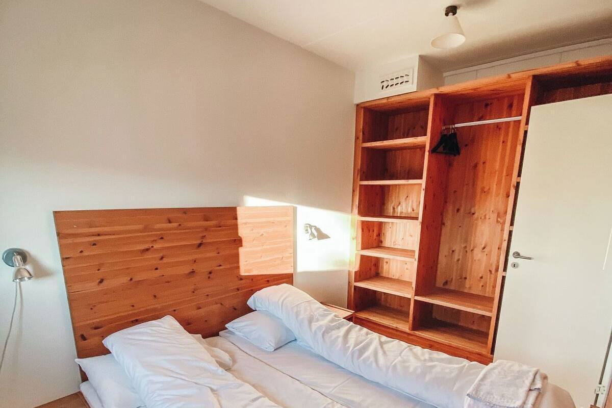 A double bed with white linens, a wooden headboard, and a wooden wardrobe with shelves.