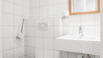 A small, modern bathroom with white tiles, a white sink, a mirror, and a toilet.