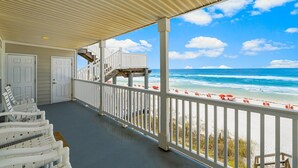 Eine überdachte Veranda mit weißen Geländern und Blick auf den Strand, sowie Strandstühle.