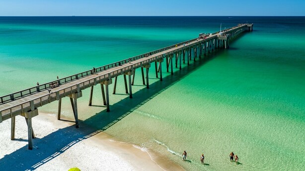 Eine Pier, die sich in türkisfarbenes Wasser erstreckt, mit blauem Himmel.