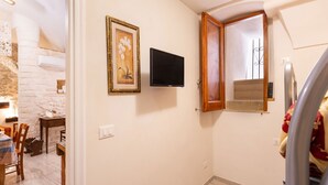 A room with a television mounted on the wall, a wooden-framed window, and a stone wall in the background. - 3929 Casa Ferrante by Barbarhouse (Vieste)