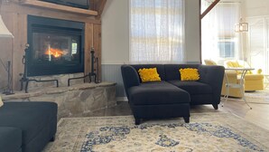 Un salon avec une cheminée, un canapé avec des coussins jaunes et un tapis à motifs.
