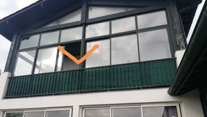 Un edificio de dos pisos con ventanas amplias y un balcón verde.