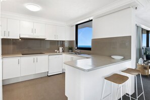 A modern kitchen with white cabinetry, a built-in dishwasher, a large window, and a bar area with stools.