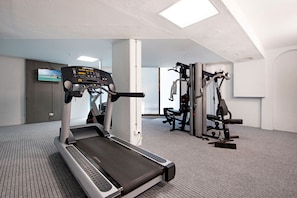 A gym with a treadmill, weight machines, and a TV screen displaying a beach scene.