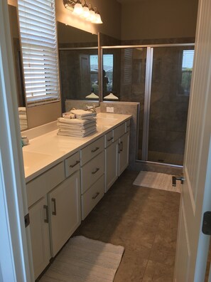Bathroom features a large mirror, countertop with towels, and a glass shower enclosure.