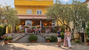 A yellow building with a covered outdoor seating area and potted plants. - Double room Pikolo with breakfast included (Sv. Filip I Jakov)