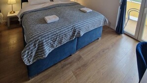 Ein Schlafzimmer mit einem Bett, zwei Nachttischlampen, einer Deckenleuchte und Blick durch eine Glastür.