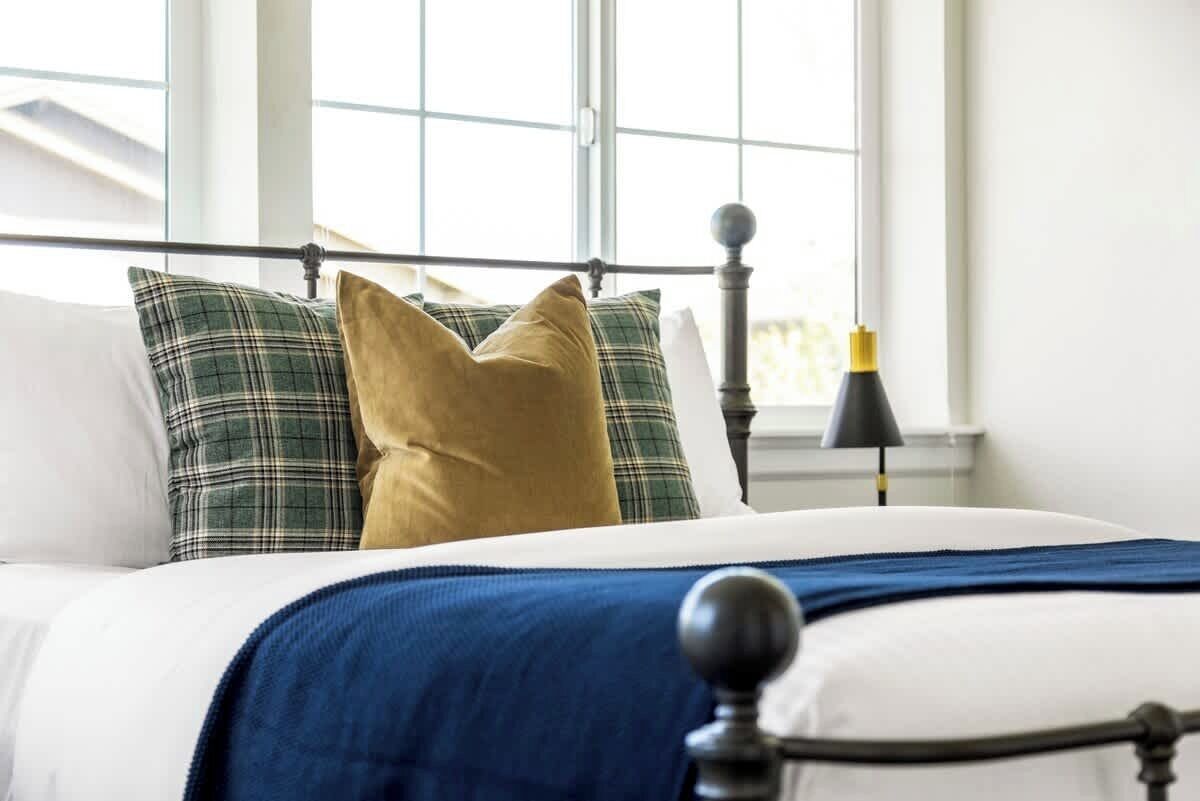 A bed with a metal headboard, white bedding, and plaid and solid-colored pillows.