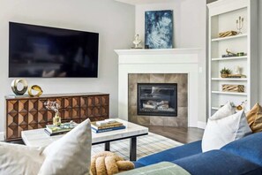 A modern living room with a fireplace, a flat-screen TV, a bookshelf, and a sofa. - Modern Elegance | Pool Table | Walkable Area (Denver)