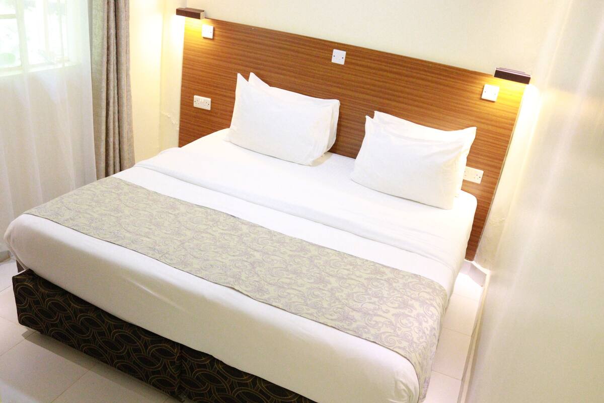 Una cama bien hecha con cabecera de madera, sábanas blancas y colcha estampada.
