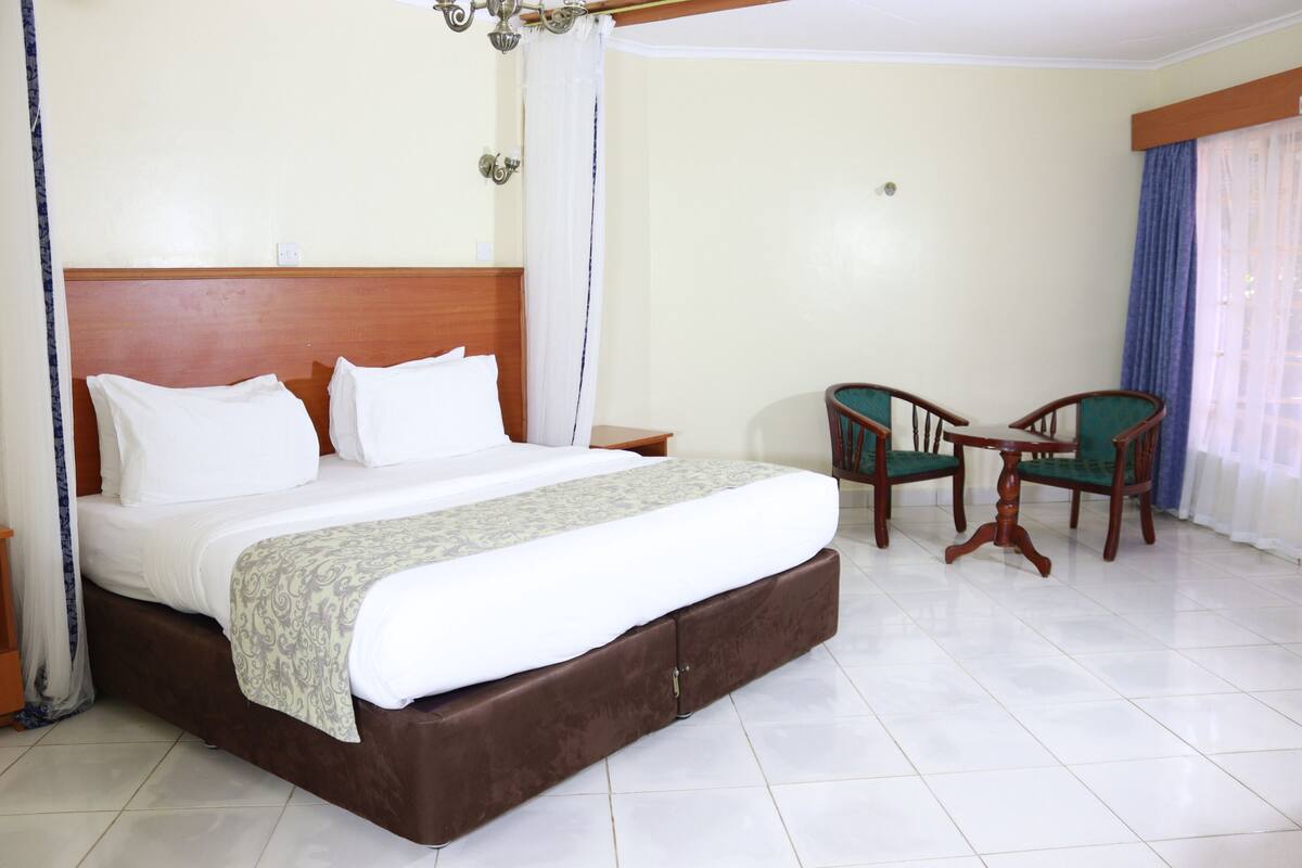 Habitación de hotel con una cama grande, dos sillas, una mesita y una ventana con cortinas.