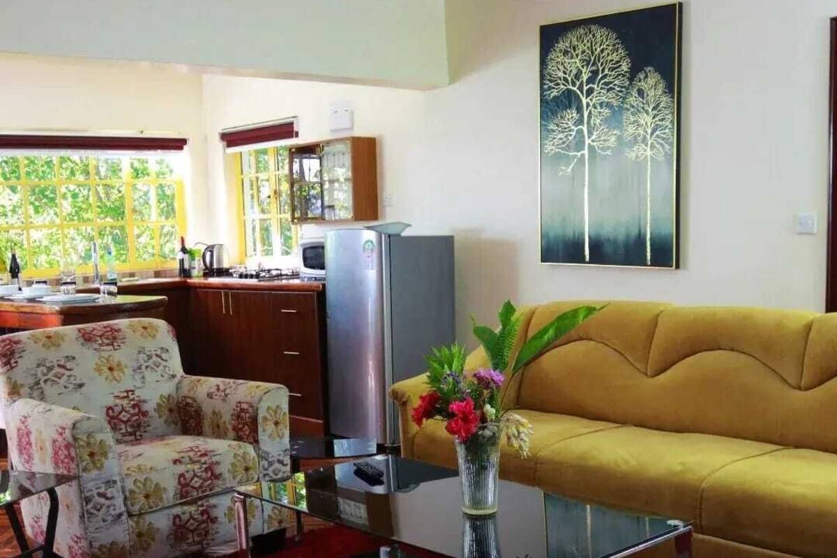 Una sala de estar con sofá, sillones, una mesa de centro y televisor. Hay una zona de cocina con armarios y un refrigerador.