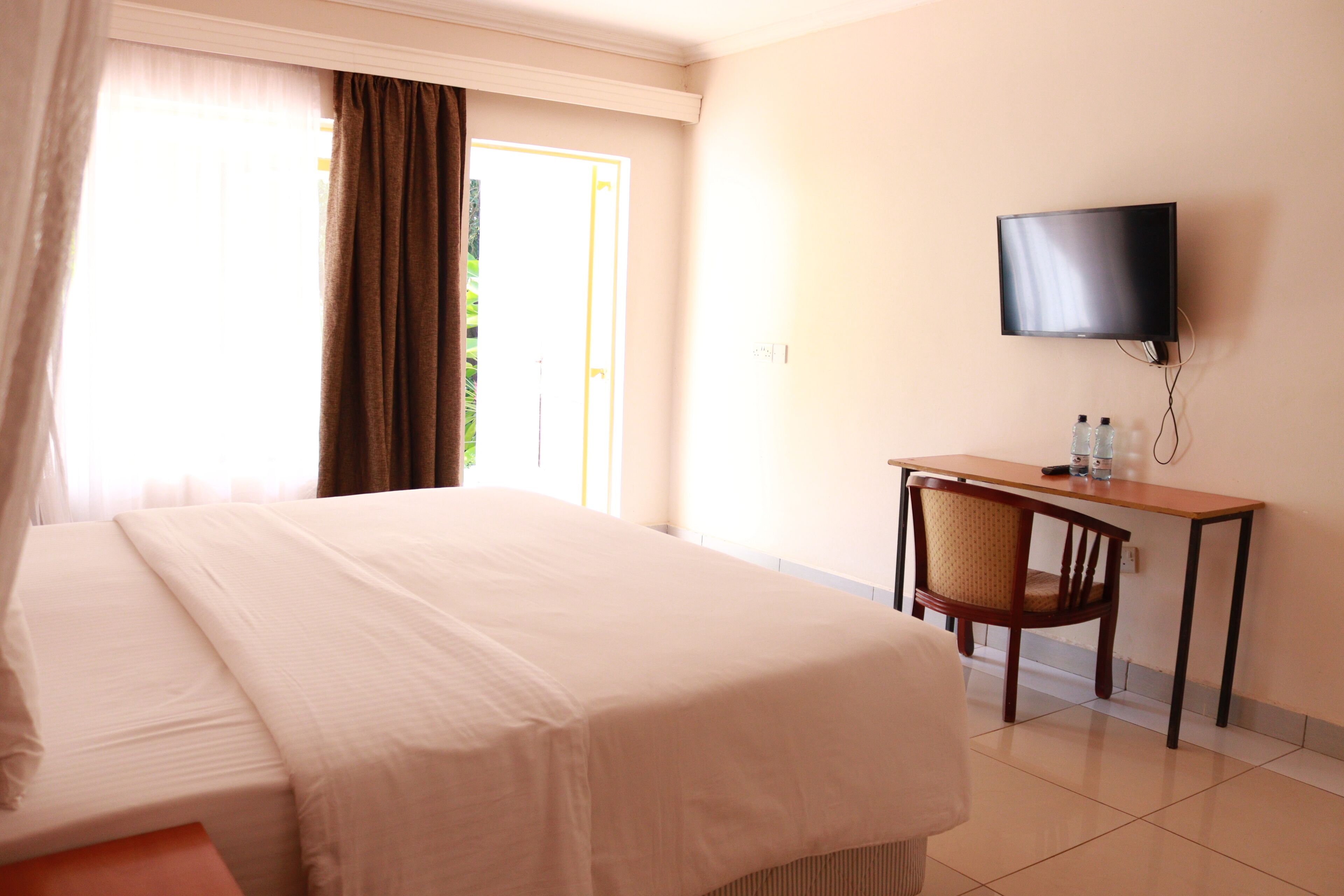 Une chambre d’hôtel comprenant un lit, un bureau, une chaise, une télévision et une fenêtre avec des rideaux.