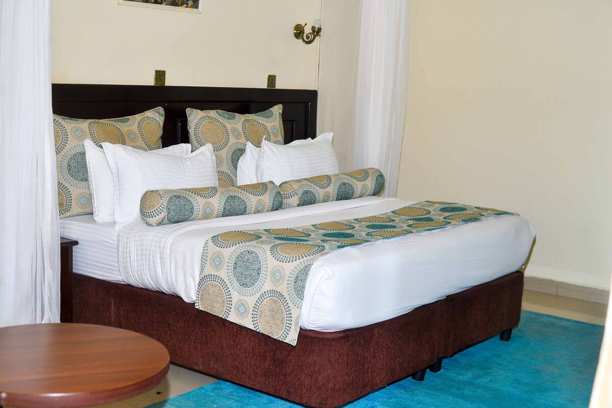 Una cama bien hecha con ropa de cama estampada, un cabecero de madera y una mesita redonda a su lado.