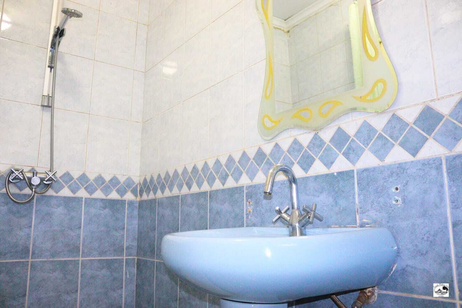 A bathroom with a blue sink, a shower, and a mirror with a yellow frame.