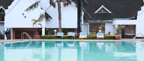 Una piscina con sillones de descanso y palmeras.