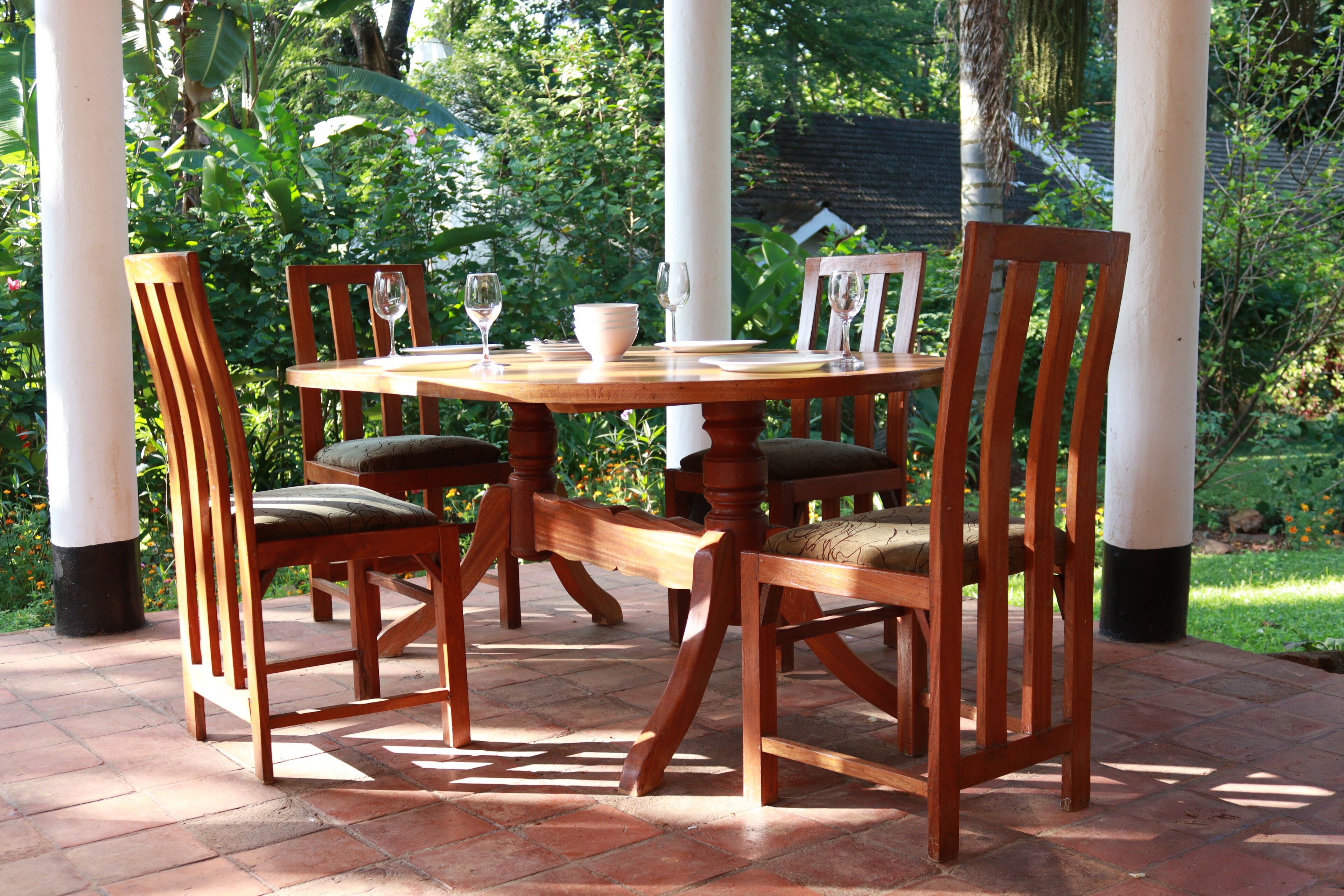 A wooden table with chairs, surrounded by greenery.