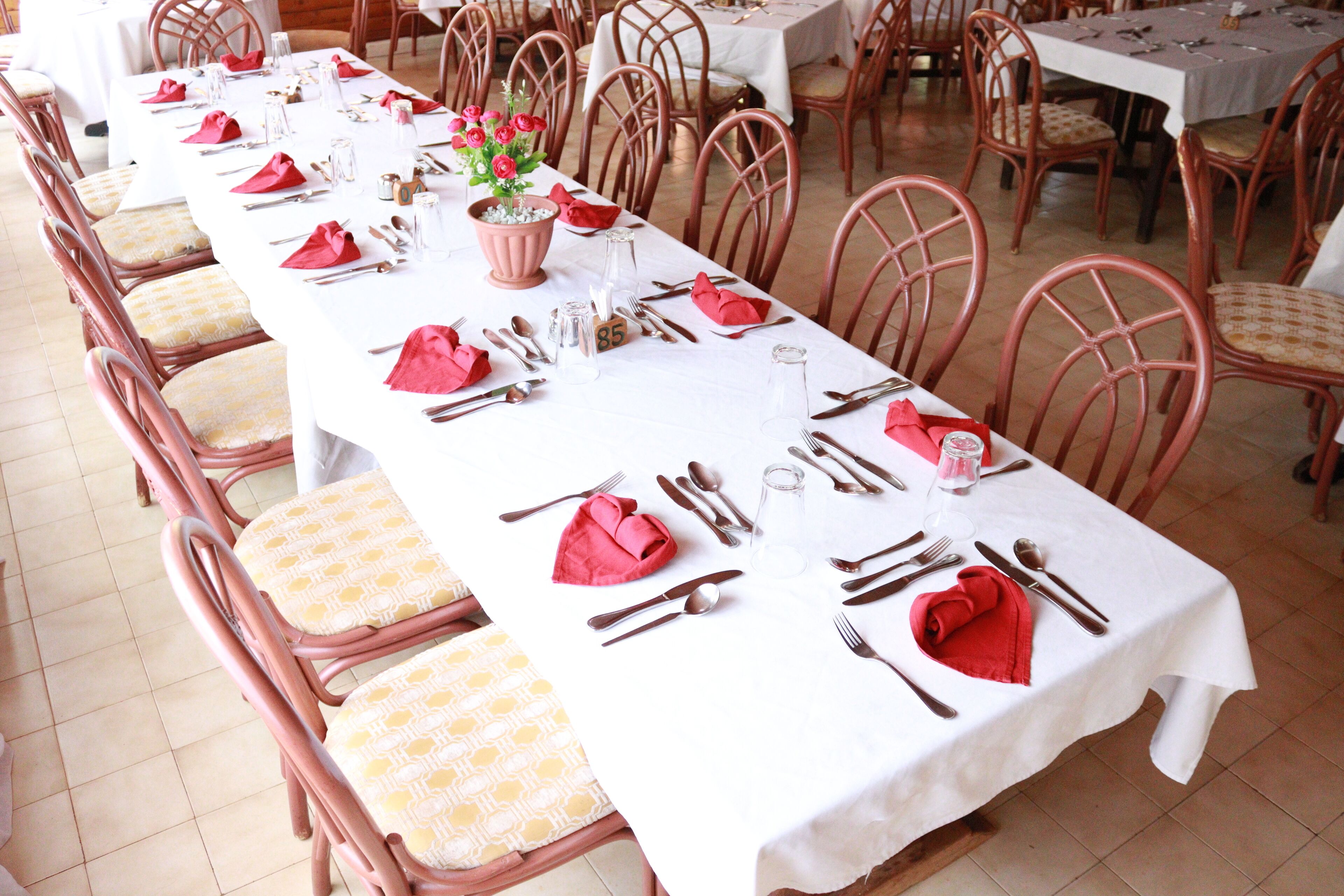 Een lange eettafel gedekt met rode servetten, bestek en een bloemstuk als middelpunt.