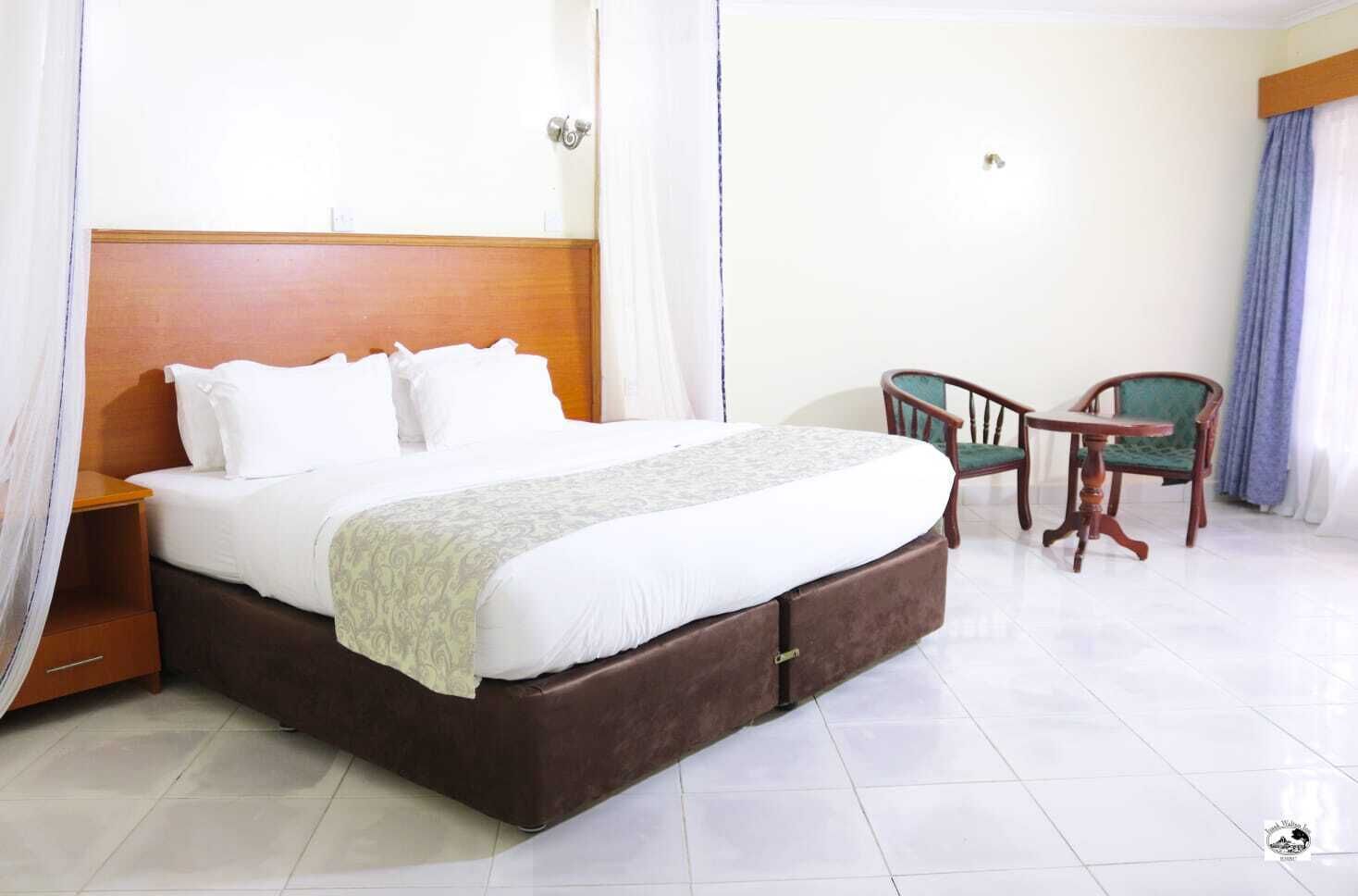 Habitación de hotel con una cama grande, un cabecero de madera, dos sillas y una mesita.