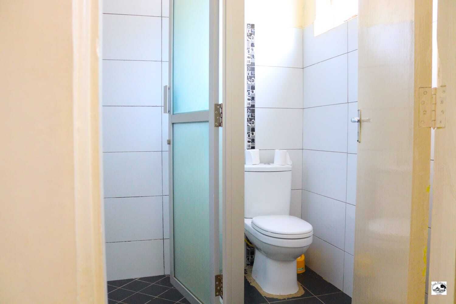 A small, narrow bathroom with white tiles, a glass shower door, and a white toilet.