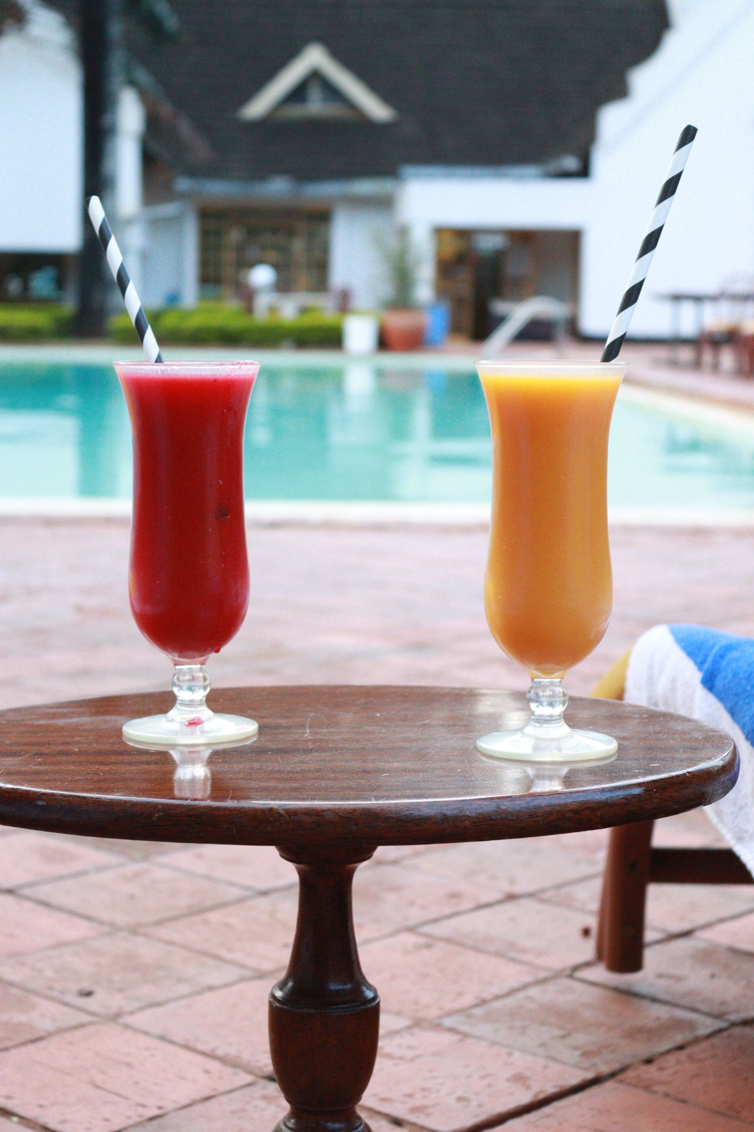 Dos bebidas sobre una mesa de madera redonda, con una piscina al fondo.