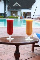 Dos bebidas sobre una mesa de madera redonda, con una piscina al fondo.