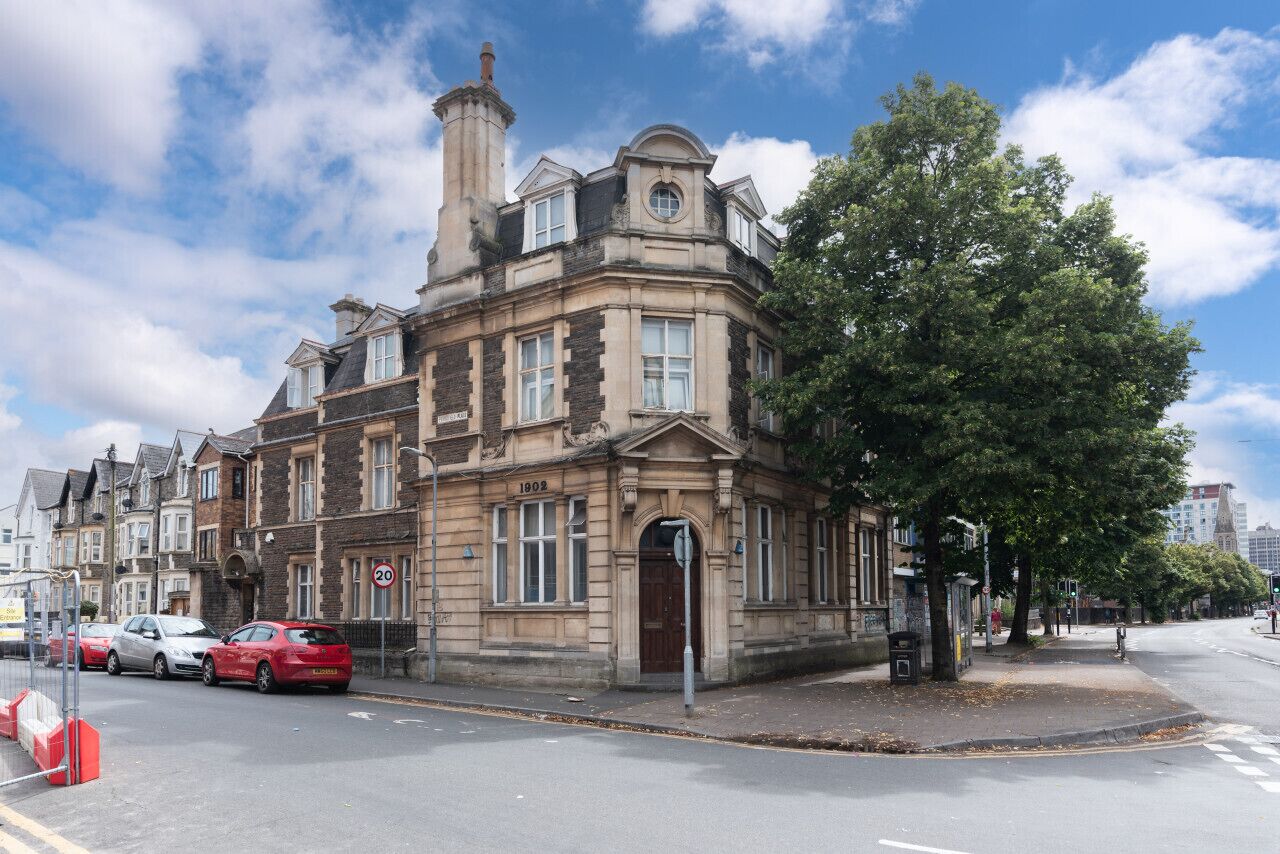A historic building with a prominent corner entrance, large windows, and a chimney.