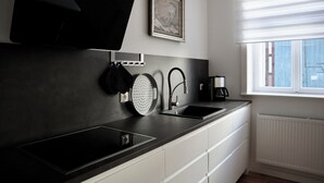 A modern kitchen with a black countertop, white cabinets, a built-in stove, a coffee maker, and a window with blinds. - 5 Ferienwohnung in Historischem Alten Gutshaus in Breetz am Fluss (Lenzen (Elbe))