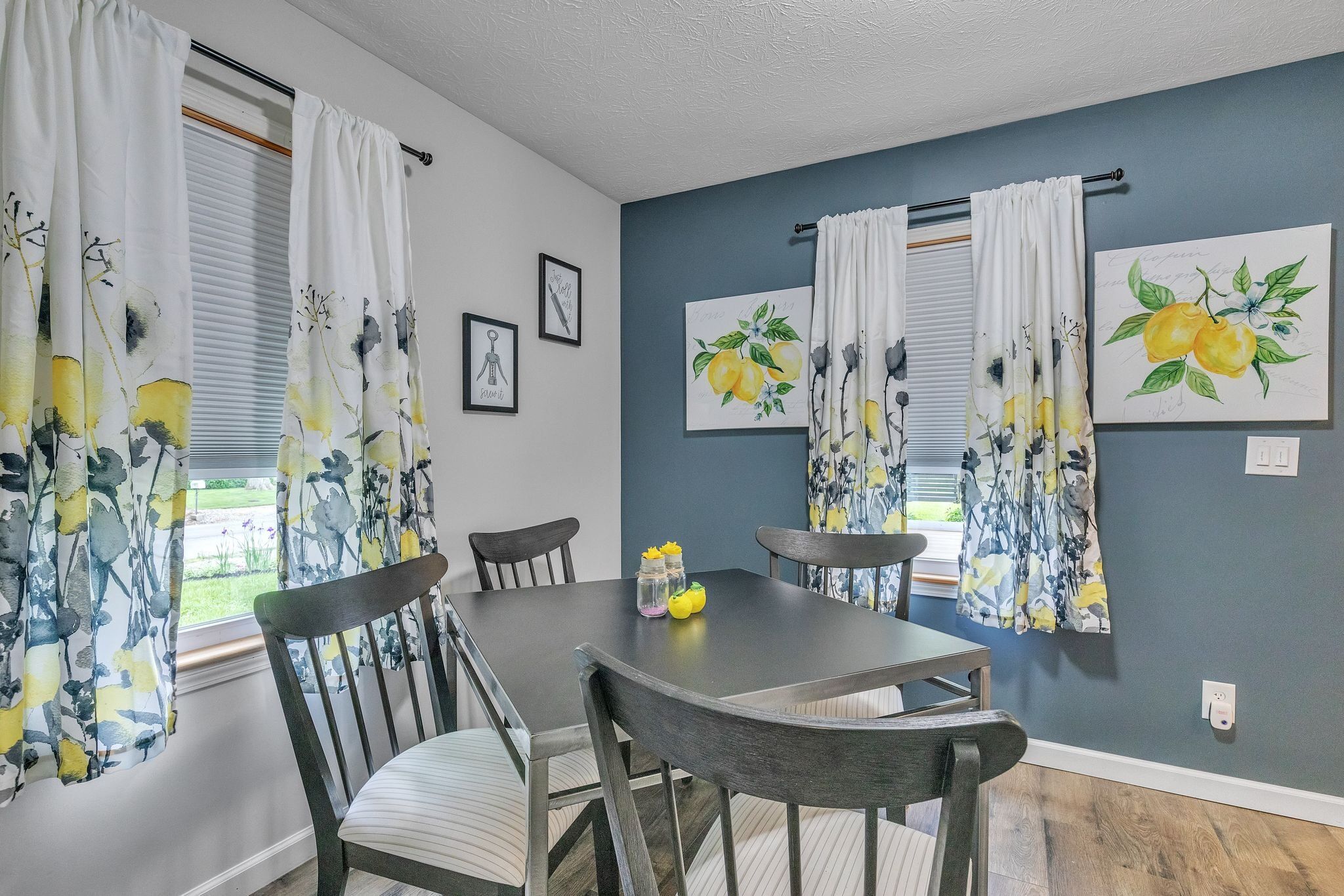 Un comedor con una mesa y sillas, una ventana con cortinas y dos obras de arte enmarcadas en la pared.