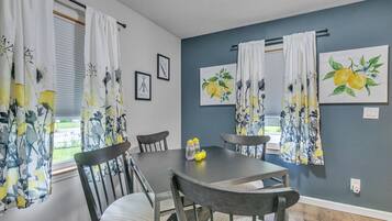 Un comedor con una mesa y sillas, una ventana con cortinas y dos obras de arte enmarcadas en la pared.