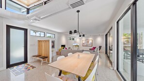 A modern, well-lit room with a large wooden table, white chairs, and a glass partition. - The Windward House 3 Bedroom Home by RedAwning (Siesta Key)