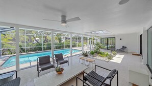 Un área de piscina interior moderna con cerramiento de vidrio, asientos y ventilador de techo.