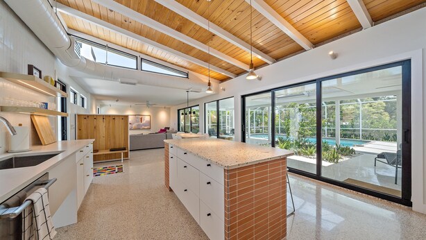 Una cocina moderna con una isla grande, vigas de techo de madera y vista a una piscina.