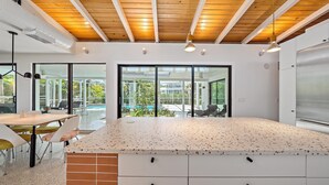 Una cocina moderna con una isla grande, armarios blancos y vistas a un área de piscina exterior.