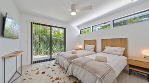 A modern bedroom with two beds, a ceiling fan, and a large window with a view of greenery. - The Windward House 3 Bedroom Home by RedAwning (Siesta Key)