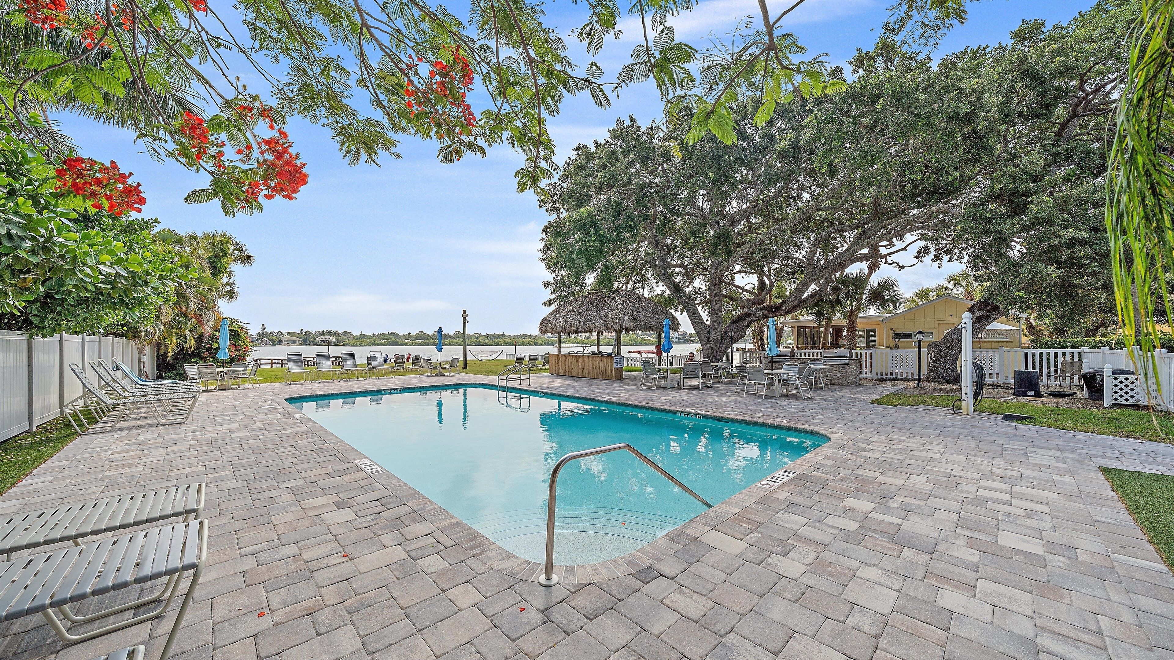 A swimming pool with lounge chairs and umbrellas, surrounded by trees and a view of the beach.