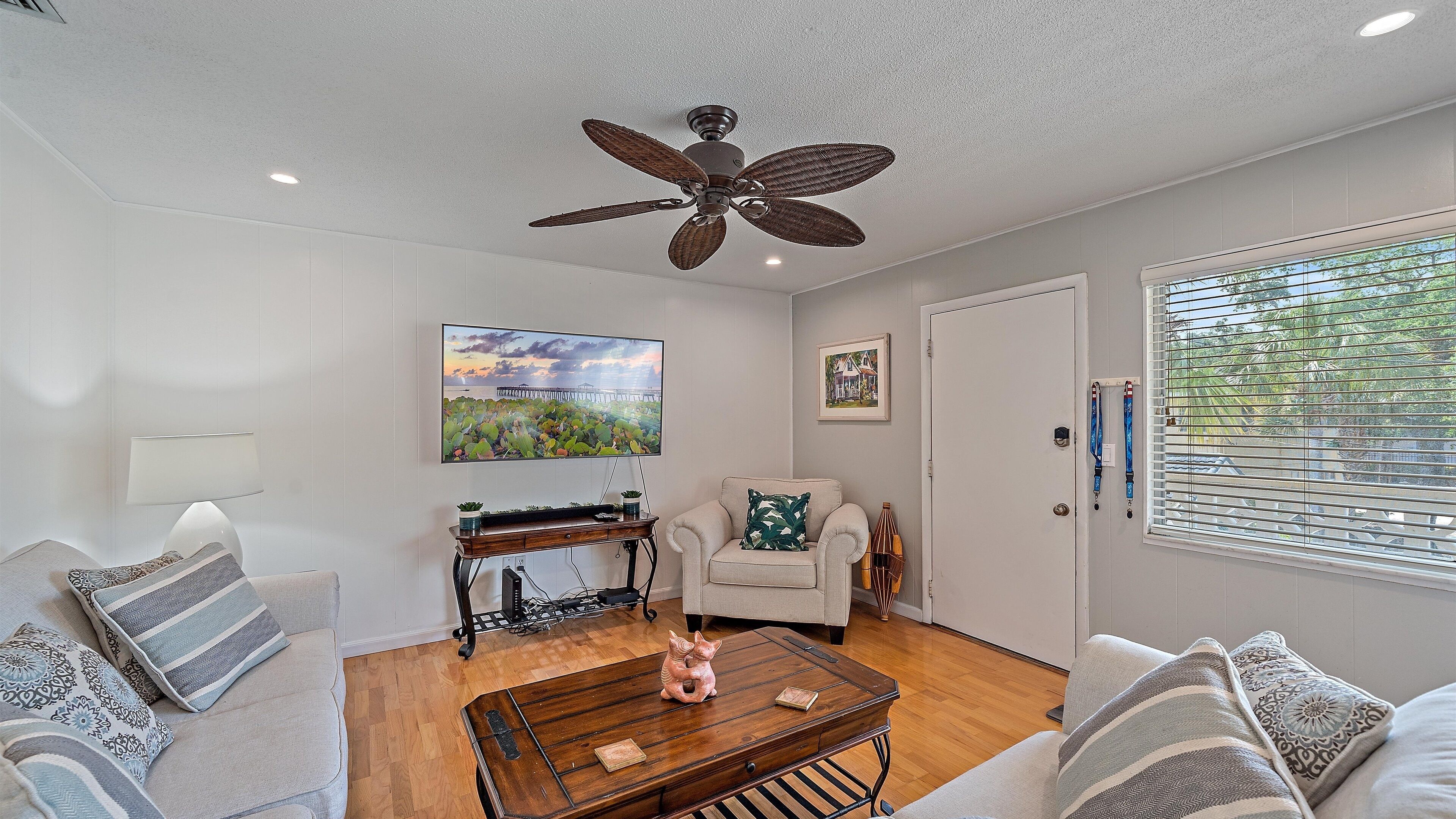 A well-lit living room with a ceiling fan, a wooden coffee table, a sofa, a chair, and a TV on the wall.