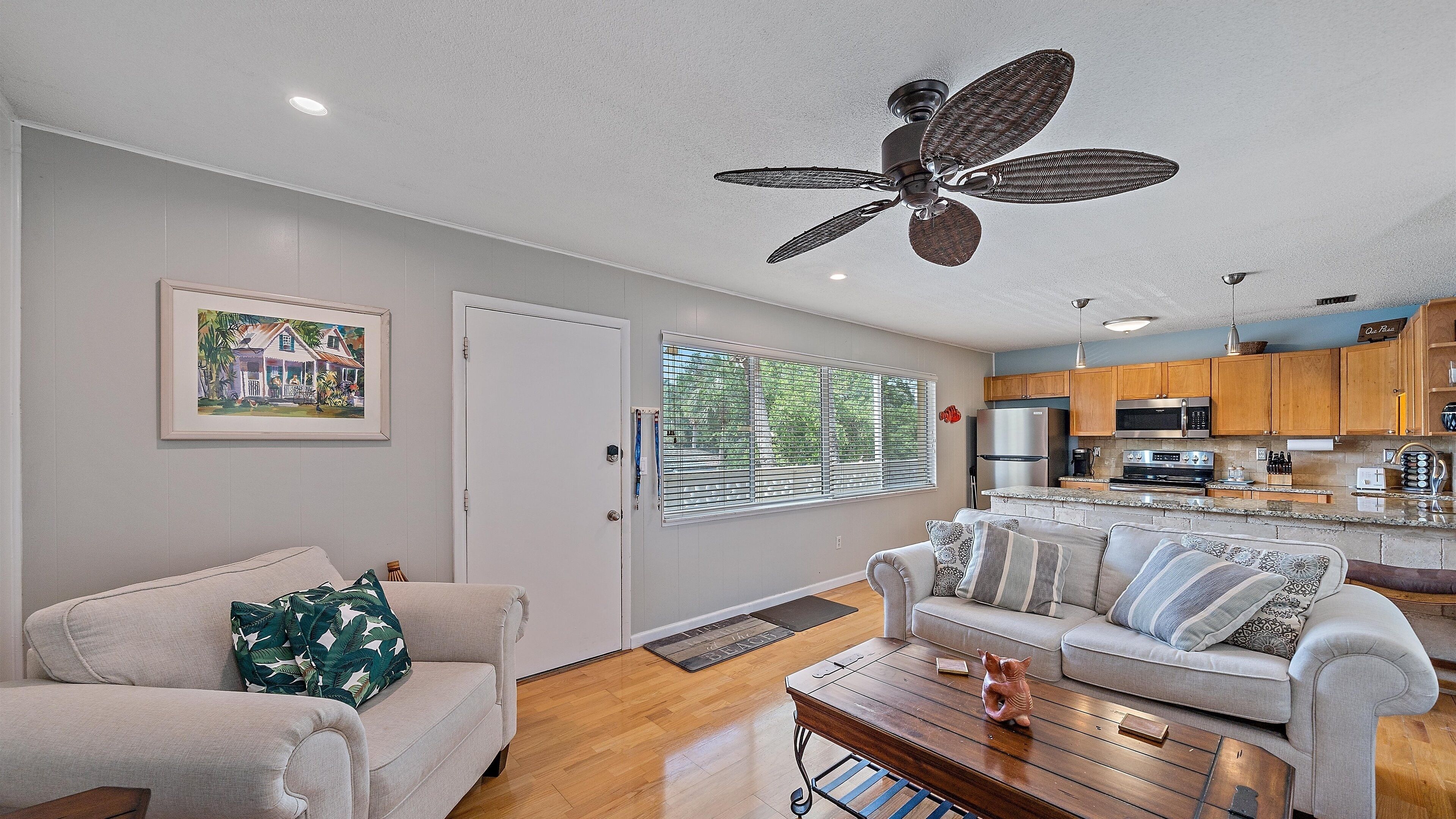 A modern living room with a ceiling fan, a kitchen with wooden cabinets, and a dining area.