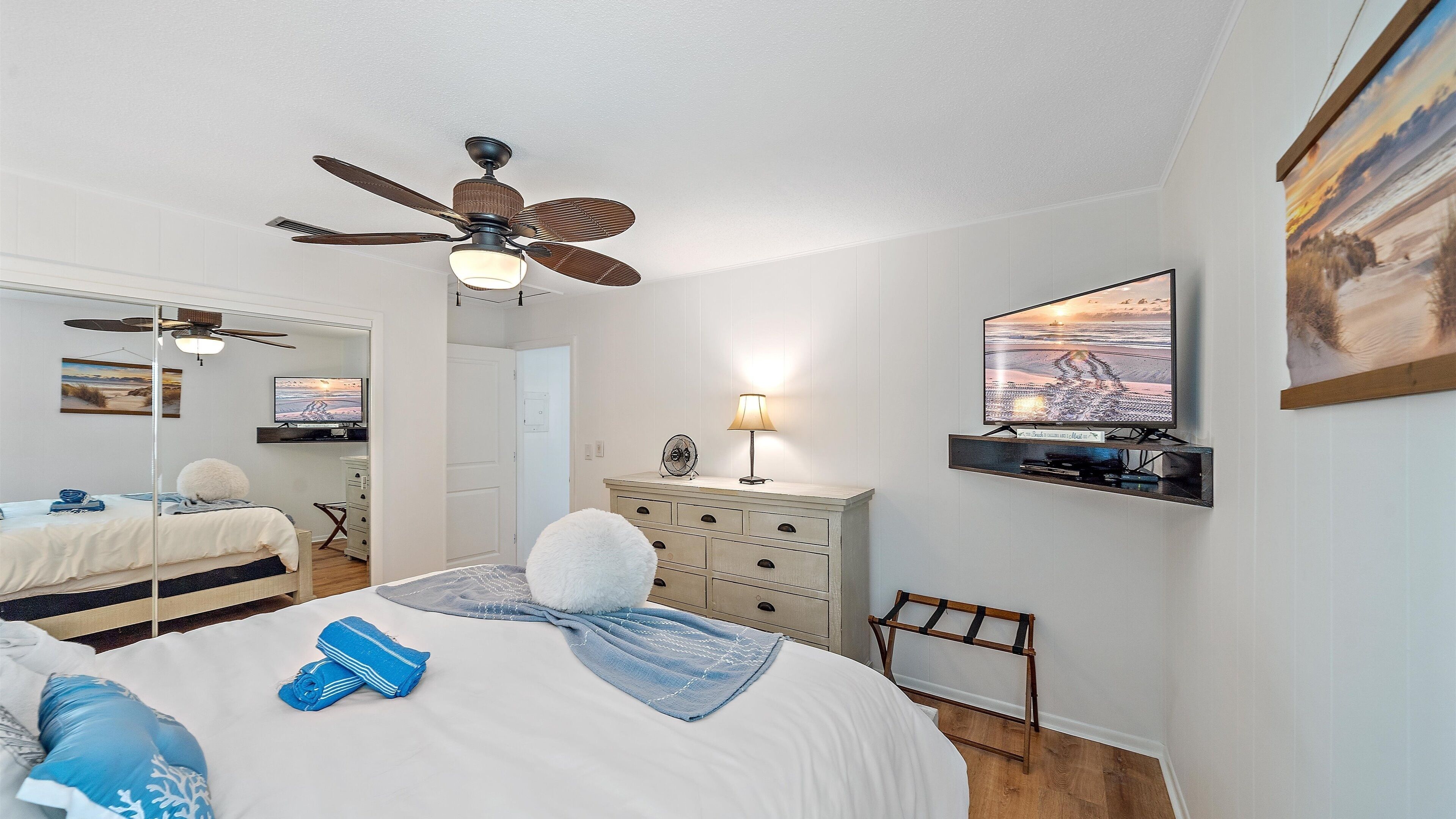 Une chambre à coucher avec un lit, un ventilateur de plafond, une télévision et une commode.
