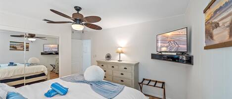 A bedroom with a bed, a ceiling fan, a TV, and a dresser.