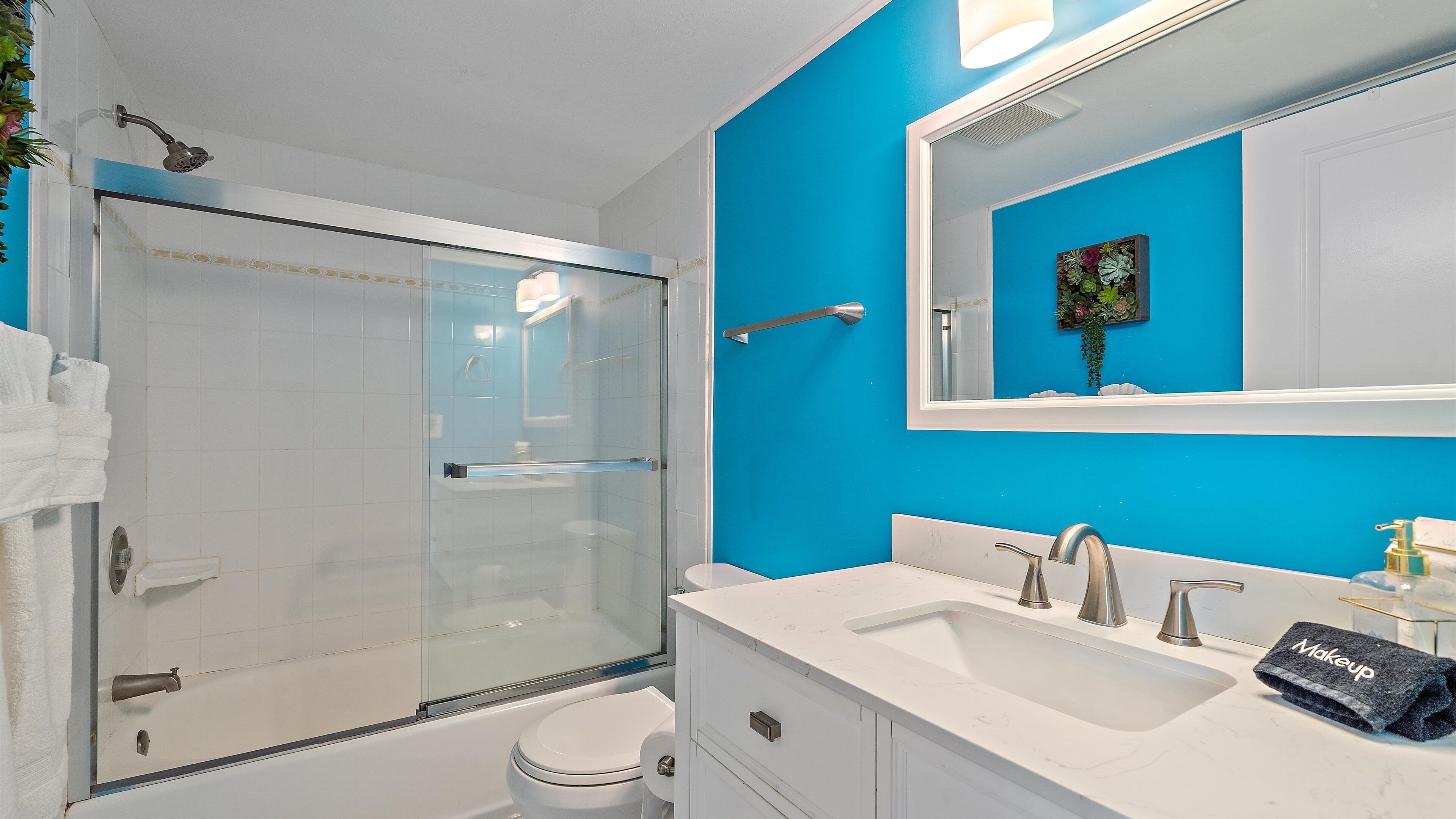 A modern bathroom with a glass-enclosed shower, a white sink with two faucets, and a large mirror above the sink.