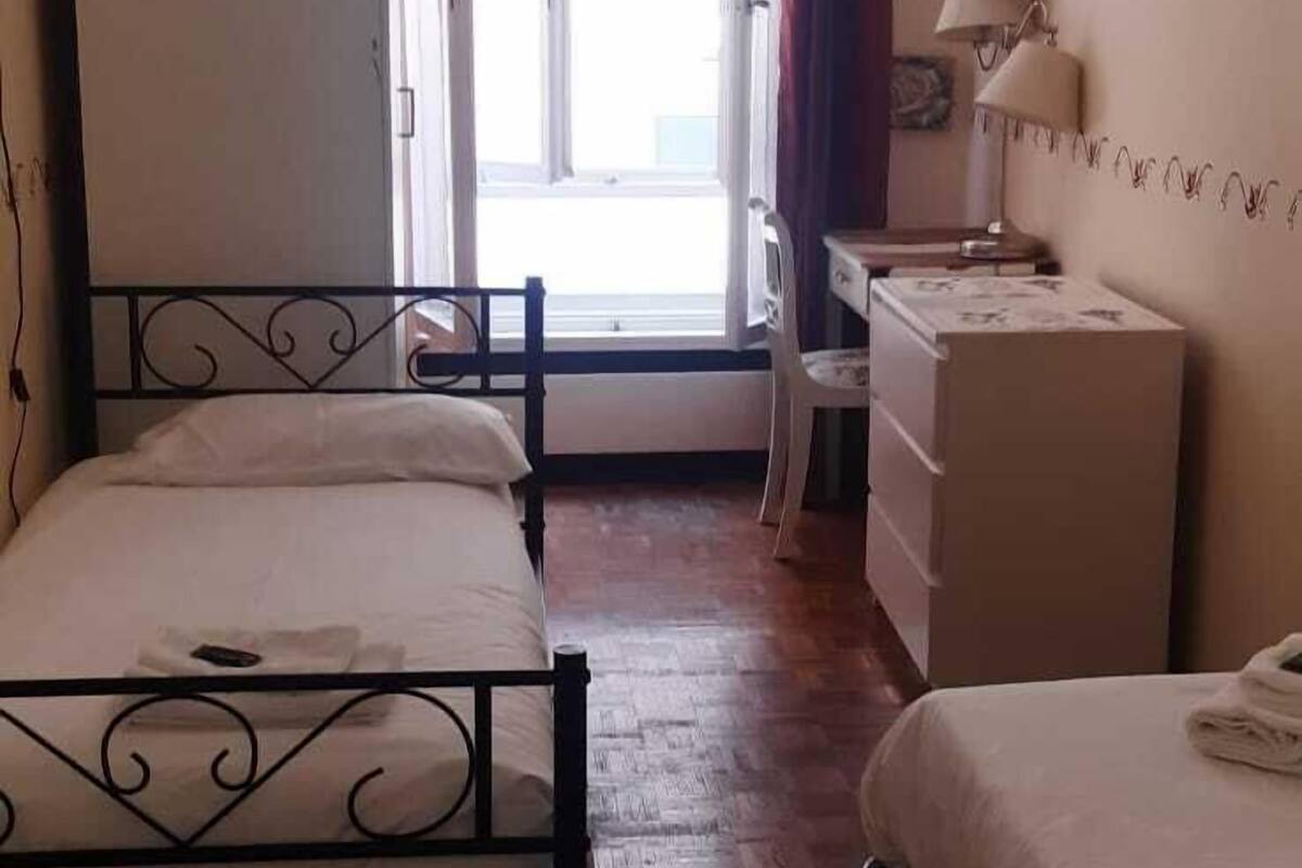 A bedroom with two beds, a desk, a dresser, and a window with curtains.